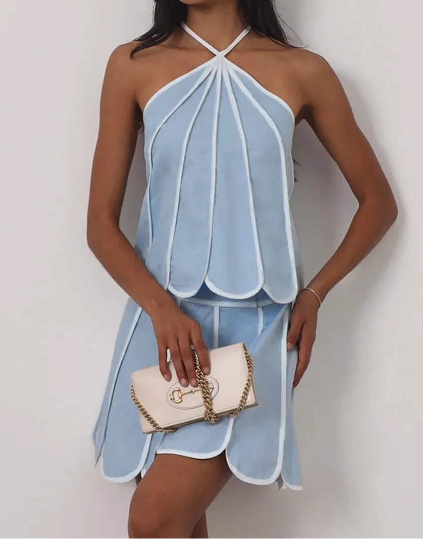 Woman wearing a light blue halter dress holding a white handbag against a plain background