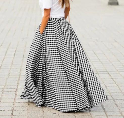 Person wearing a long black and white checkered skirt on a light stone pavement.