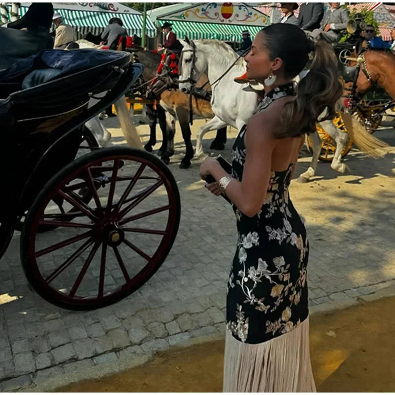 Woman in a floral dress standing next to a horse-drawn carriage with a carousel in the background.