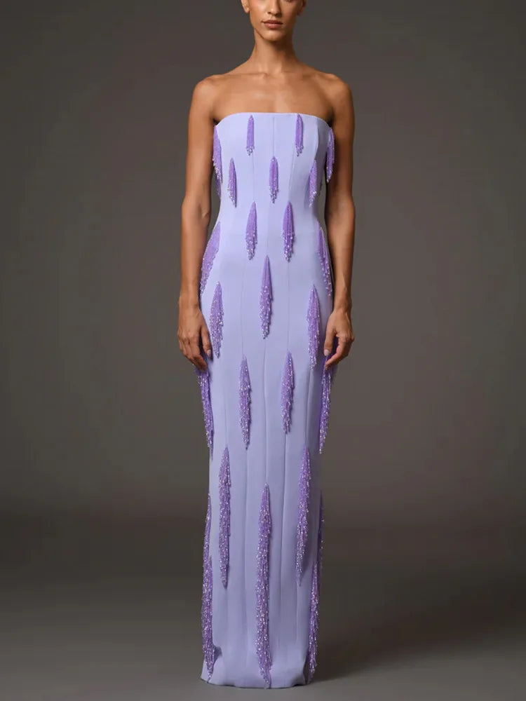 Woman wearing a strapless purple evening gown with tassel beads on a gray background