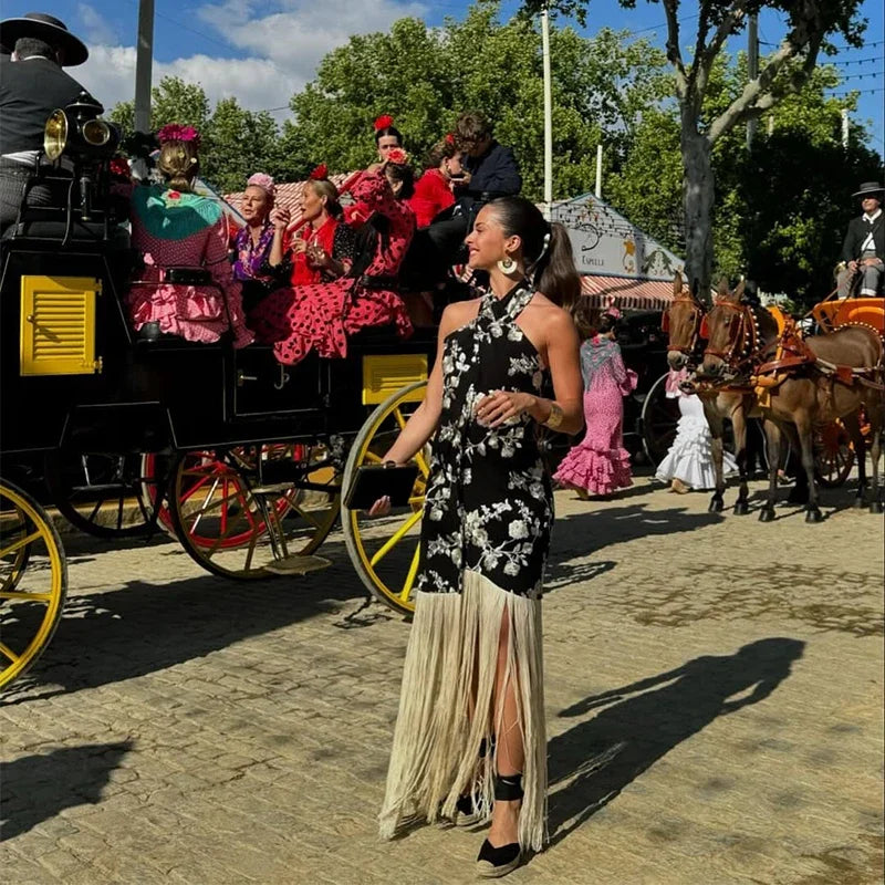 Woman in a black and white dress walking past a horse-drawn carriage with people in colorful dresses.