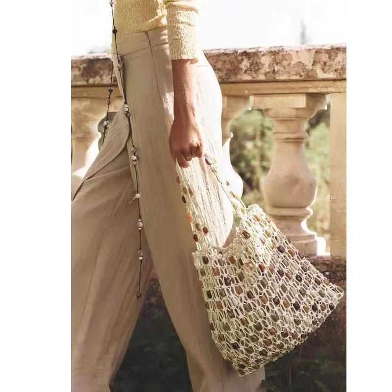 Person holding a woven bag outdoors with classical architecture in the background