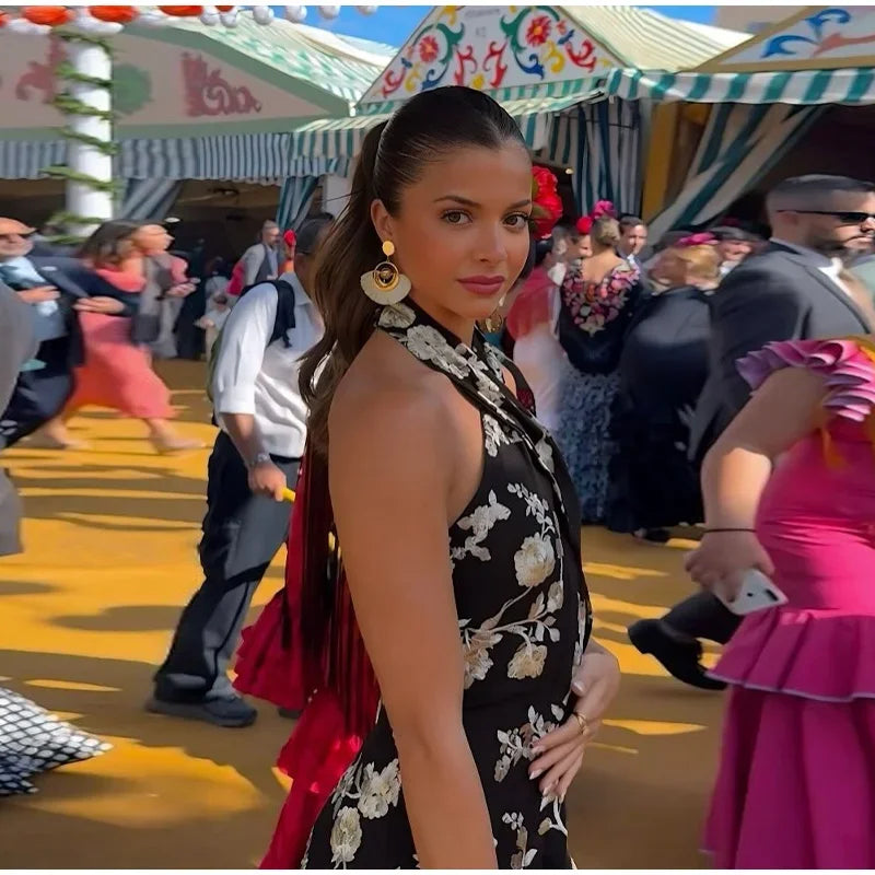 Woman in a black floral dress at a festive outdoor event with colorful tents.
