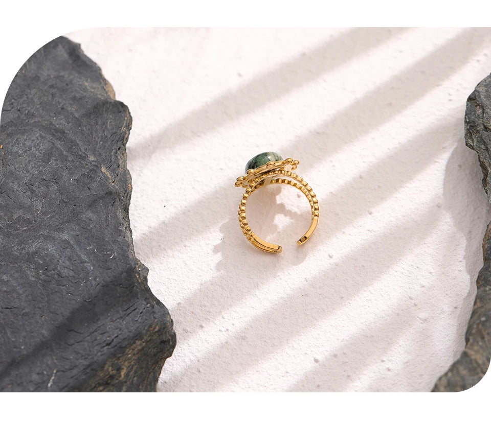 Gold ring with a green gemstone on a textured white surface with gray stones.