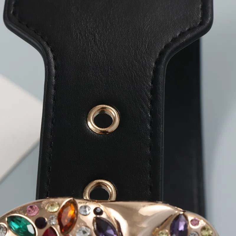 Close-up of a black leather strap with a gold buckle featuring colorful gemstones.