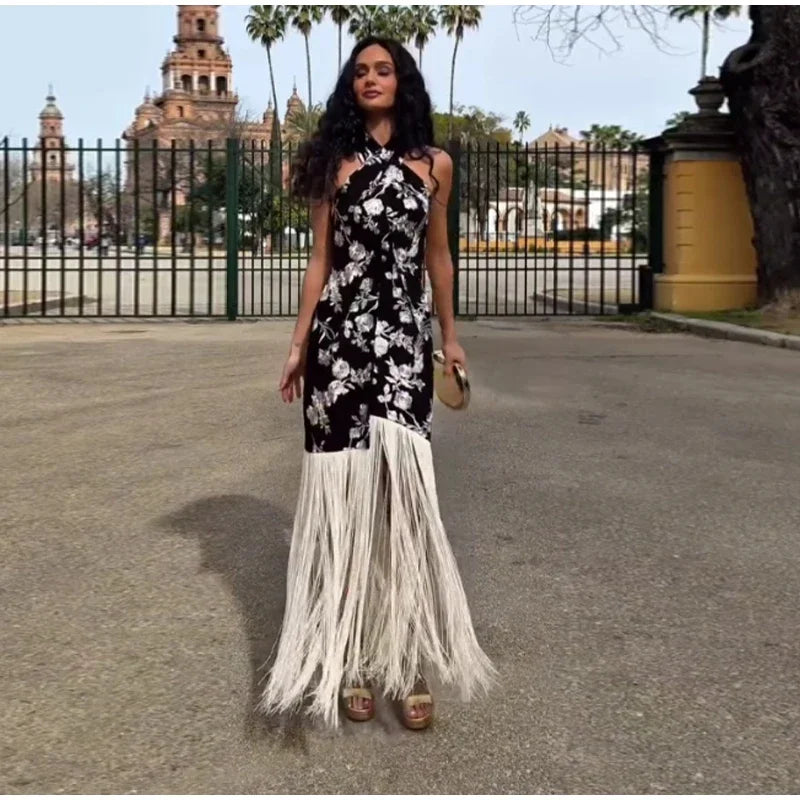 Woman wearing a black floral dress with white fringe in an outdoor setting.