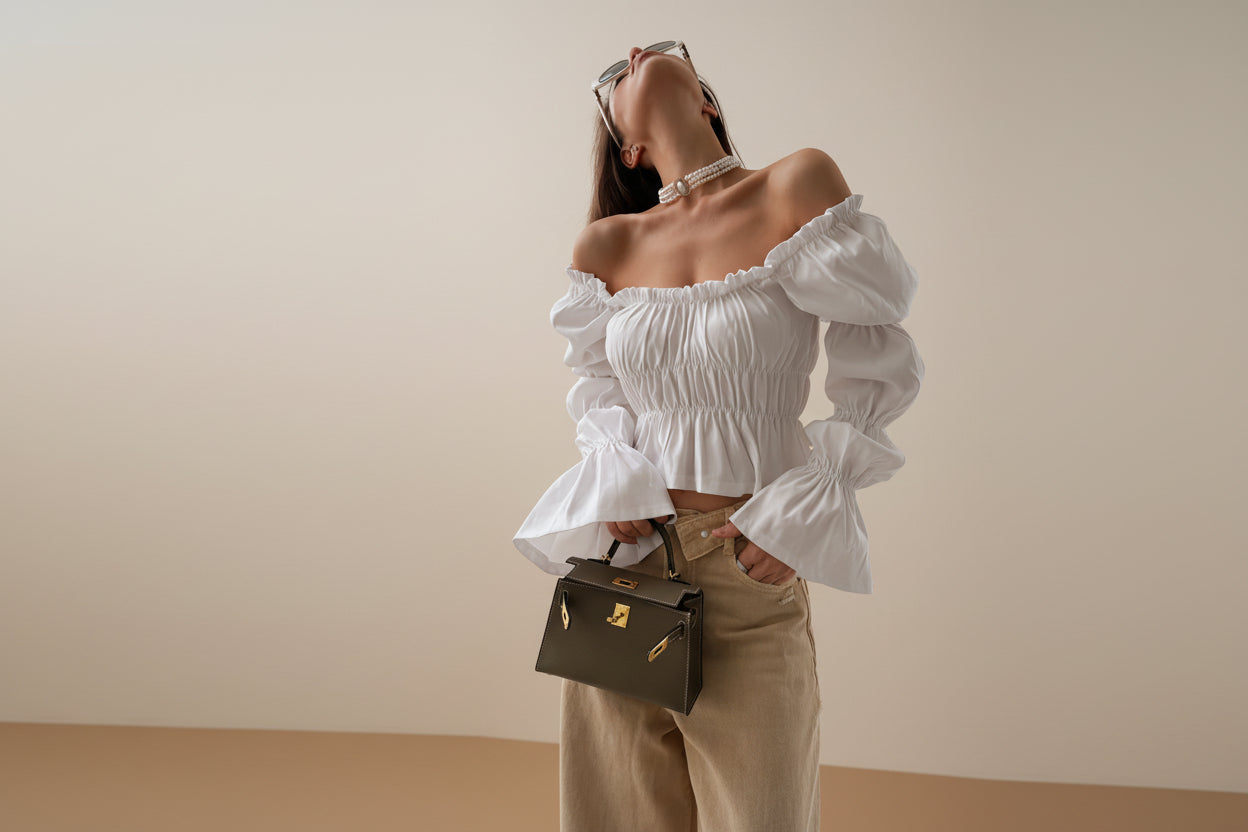 Woman wearing a white off-shoulder top with puffed sleeves, holding a brown handbag.